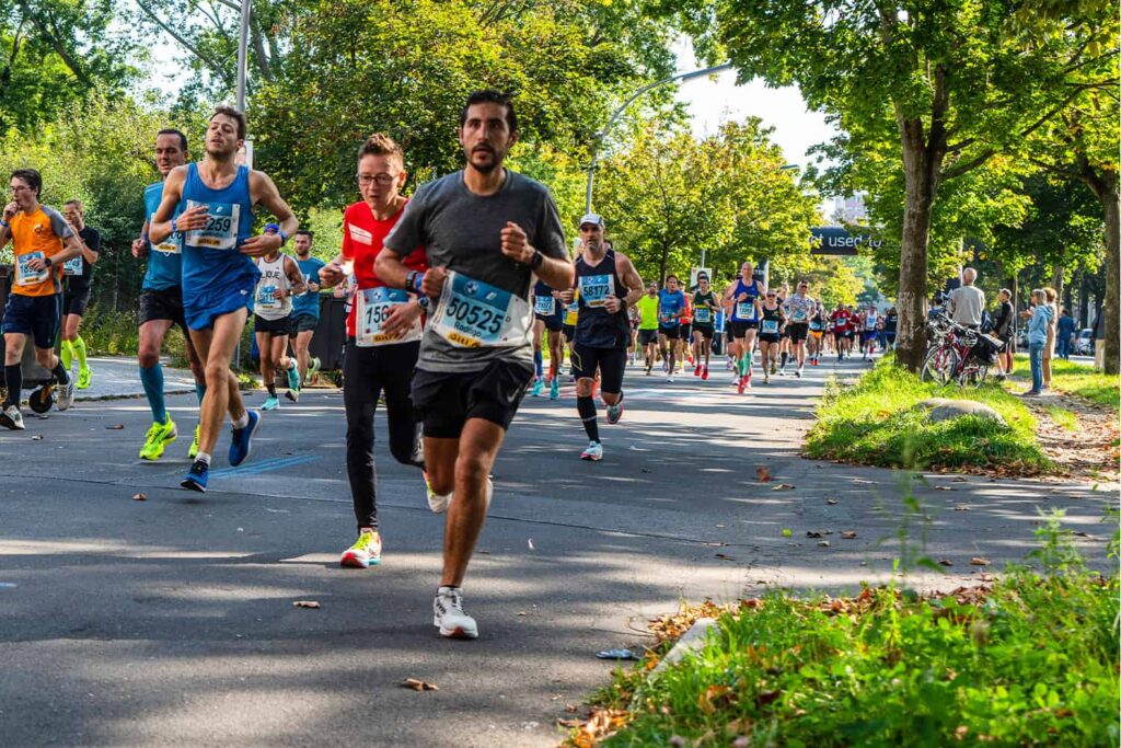 Un groupe de runners traversent une rue ombragée d'arbres, durant le Marathon de Berlin