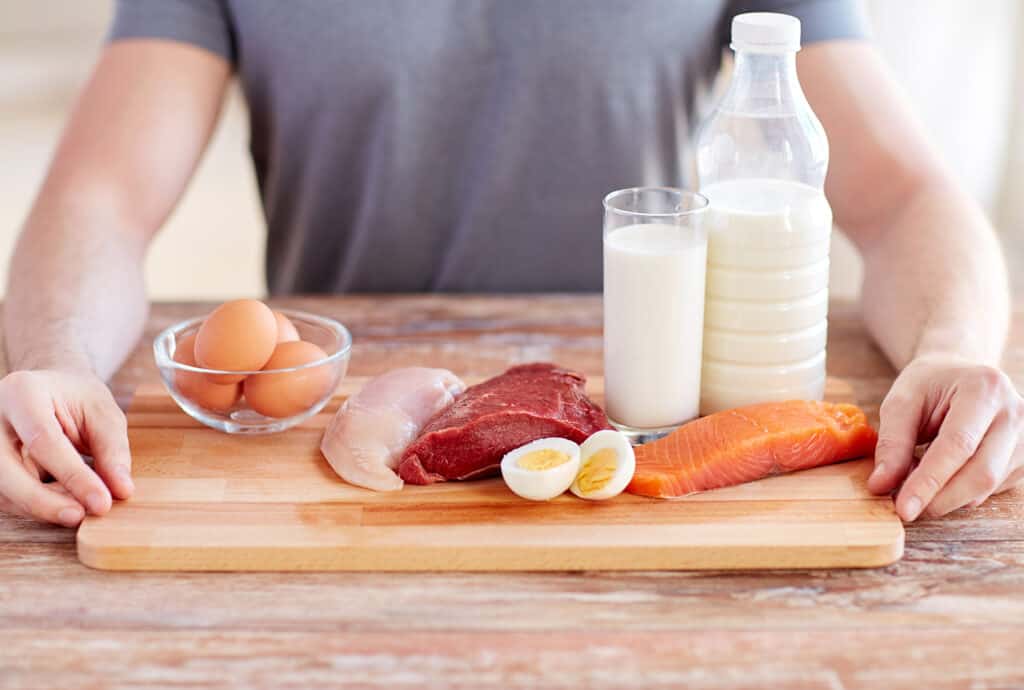 gros plan de mains masculines avec des aliments riches en protéines sur une planche à découper (œufs, poisson, viande)