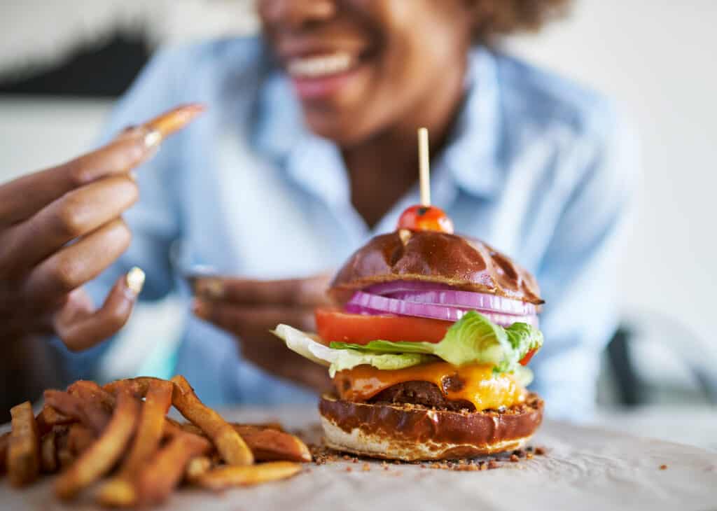perdre du poids ne veut pas dire se priver. Ici, une athlète déguste un burger vegan avec des frites et légumes