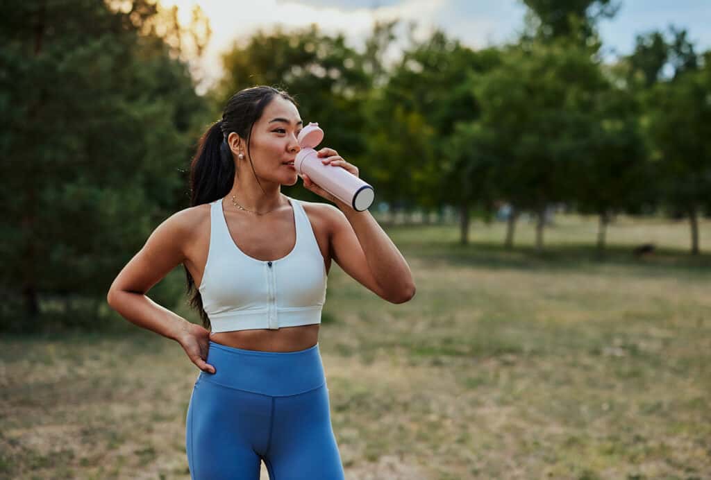 femme sportive se reposant après une séance d'entraînement dans le parc et buvant de l'eau