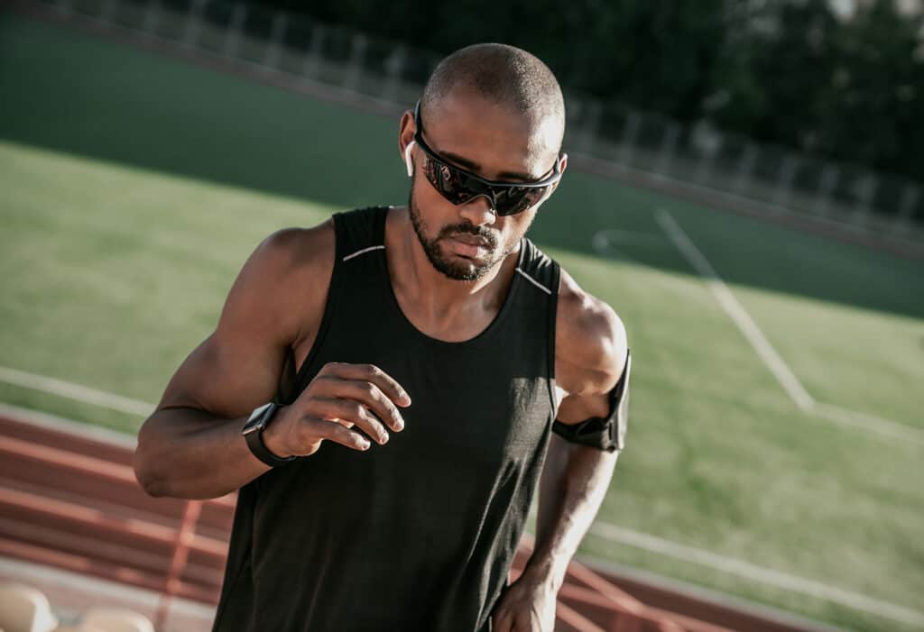 Gros plan d'un athlète masculin portant des lunettes de soleil et des écouteurs qui monte les escaliers d'un stade.