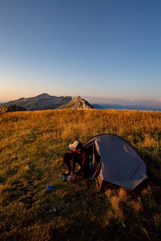 Un homme assis près de sa tente et regardant les montagnes