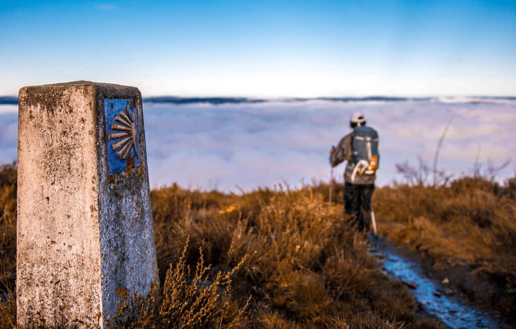 Pèlerin marchant sur le Camino de Santiago, au-dessus d'une mer de nuages en pleine nature