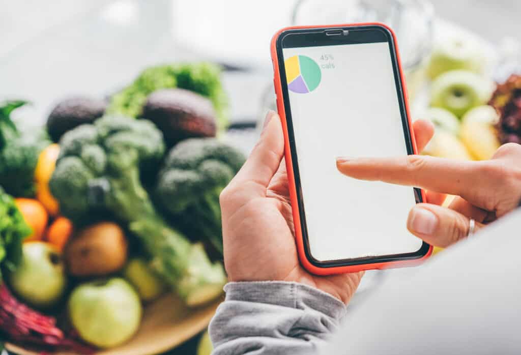 Vue de dessus d'une fille tenant un smartphone avec une application de calcul de calories sur une table de cuisine près de légumes frais