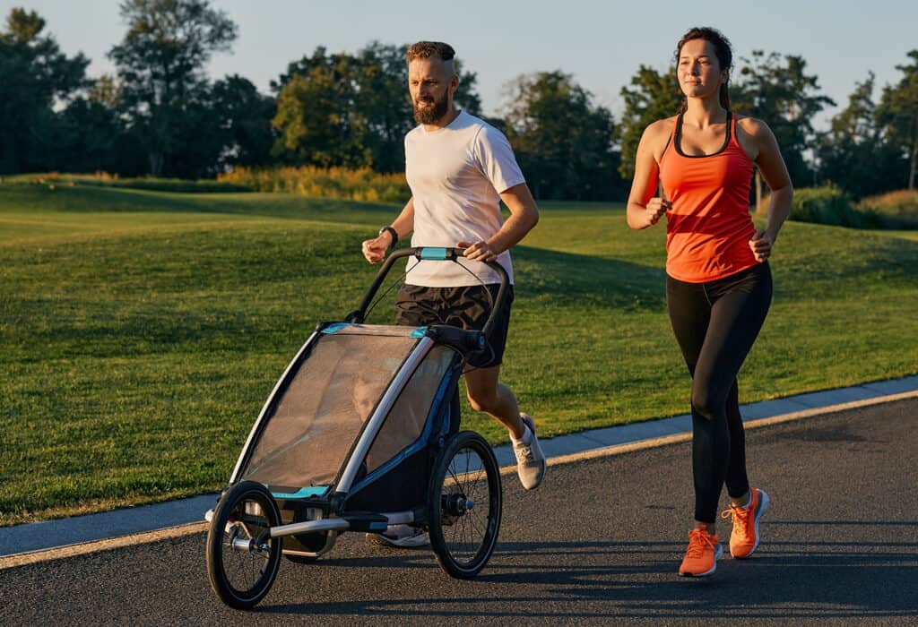Jeune famille avec leur enfant dans une poussette de jogging lors d'une course dans un parc.