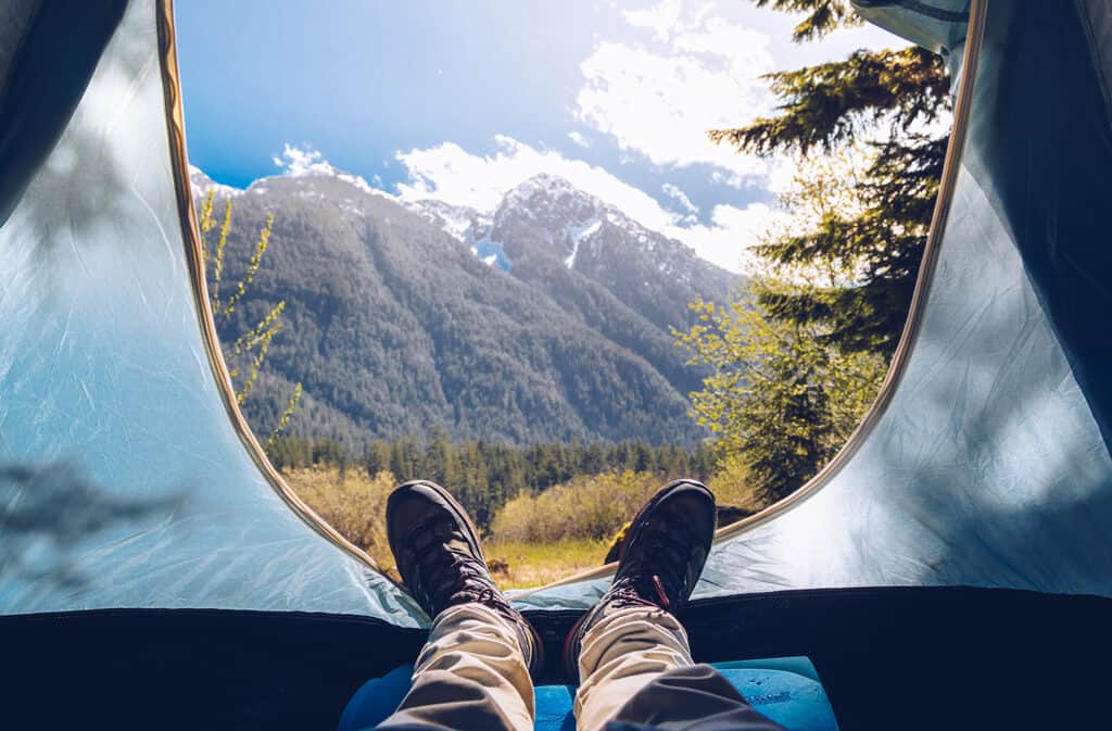 homme allongé dans une tente regardant les montagnes