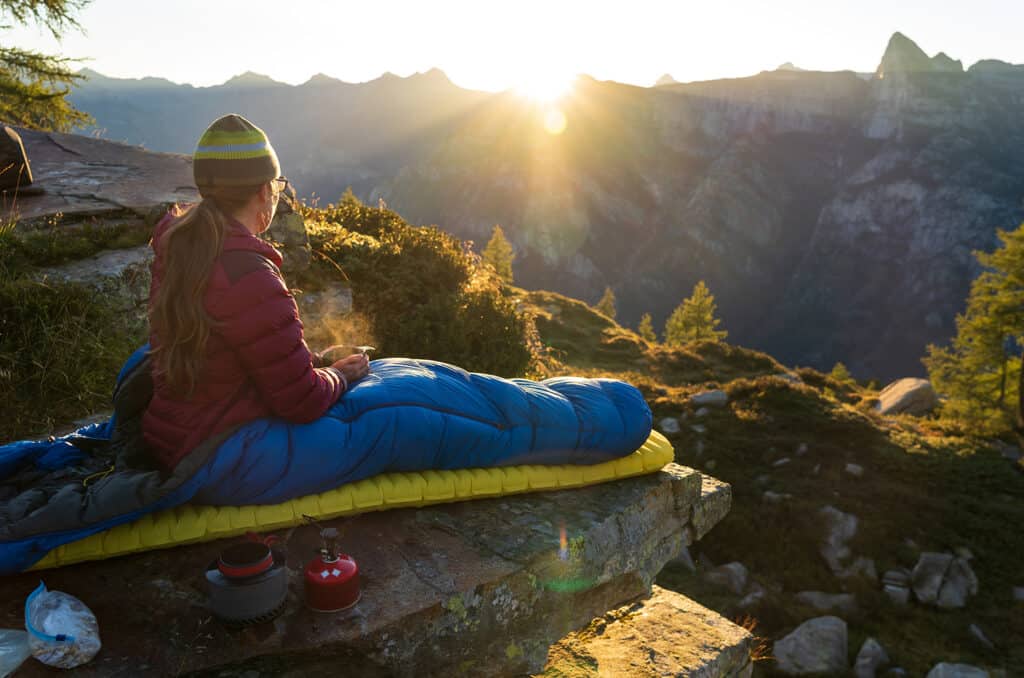 Une femme prenant son petit-déjeuner depuis son bivouac par une belle matinée en montagne