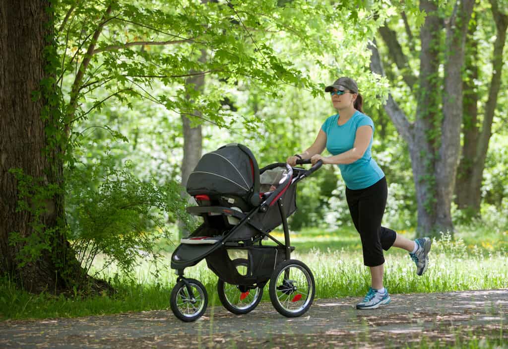 Jeune mère courant en poussant une poussette dans un parc